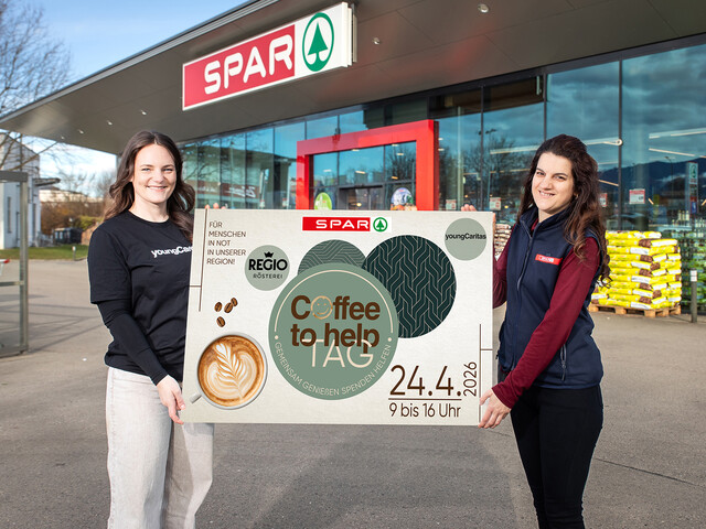 Zwei Frauen halten vor einem SPAR-Markt ein Plakat für den Coffee to help Tag am 24.4.2026 mit youngCaritas.