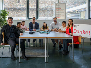 Gruppe sitzt im Lerncafé an einem Tisch bei der Übergabe einer Spende für die Caritas Lerncafes.