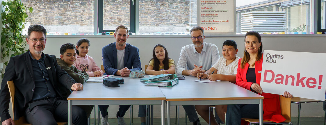 Gruppe sitzt im Lerncafé an einem Tisch bei der Übergabe einer Spende für die Caritas Lerncafes.