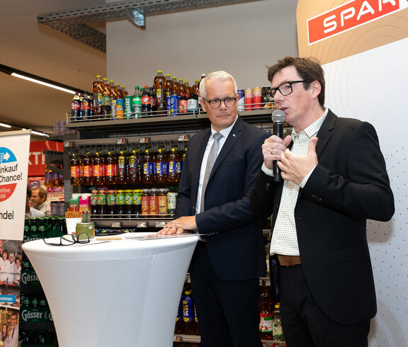 SPAR-Vorstandsvorsitzender Hans-Jürgen F. und ein weiterer Mann sprechen vor einem Regal mit Getränken.