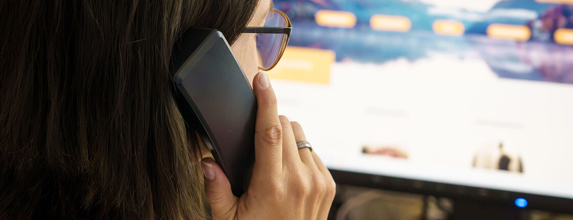 Eine Braunhaarige mit Brille hält einen Telefonhörer in der Hand und sieht dabei auf den Bildschirm, auf dem man die Website der Telefonseelsorge Österreich leicht verschwommen sieht.
