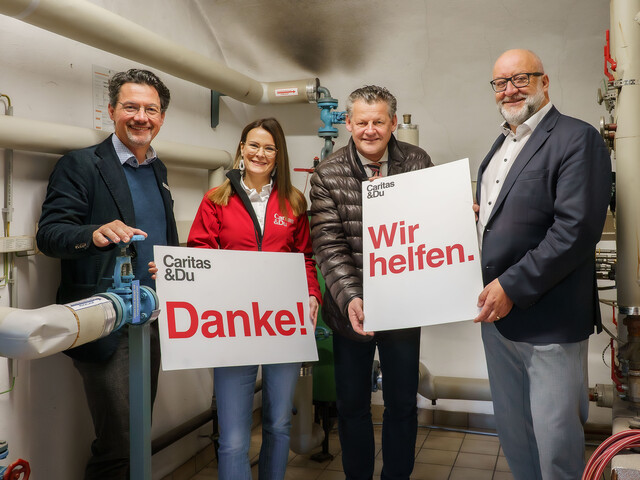 Stadtwerke-Vorstand Erwin Smole, Bürgermeister Christian Scheider, Caritasdirektor Ernst Sandriesser sowie Roberta Striedinger halten zwei Schilder mit "Danke" und "Wir helfen" im Heizungskeller der Wohnungslosentagessätte "Eggerheim".