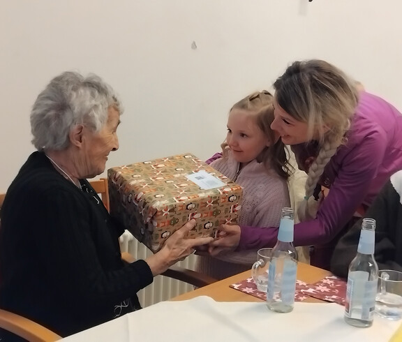 Bewohner*in erhält ein verpacktes Geschenk von einem Mädchen, begleitet von einer Erwachsenen.