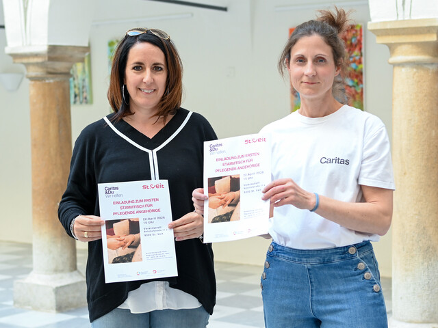 Frau Greiler von der Stadt St.Veit und Verena Wernbacher von der RegionalCaritas halten Flyer zum Pflegestammtisch für pflegende Angehörige in St. Veit.