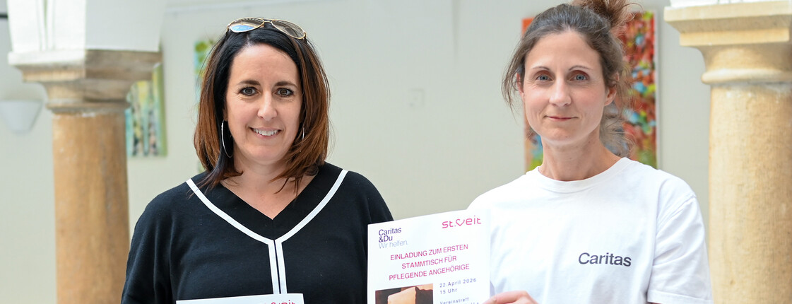 Frau Greiler von der Stadt St.Veit und Verena Wernbacher von der RegionalCaritas halten Flyer zum Pflegestammtisch für pflegende Angehörige in St. Veit.