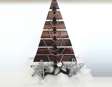 Ein Weihnachtsbaum aus Holz ist auf Watte und mit silberenen Sternen und Kugeln verziert vor einem weißen Hintergrund drapiert.