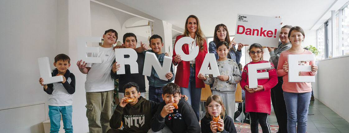 Gruppe von Kindern und zwei Erwachsenen im Lerncafé, hält Buchstaben „LERNCAFE“ und ein „Danke!“-Schild