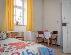 Ein Einzelzimmer eines Asyl-Quartiers. Neben einem Bett steht auch ein Tisch mit zwei Sesseln in der Ecke.