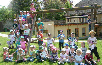 Kinder des Pfarrkindergarten Launsdorf stehen vor dem Spielturm im Garten und lächeln in die Kamera.