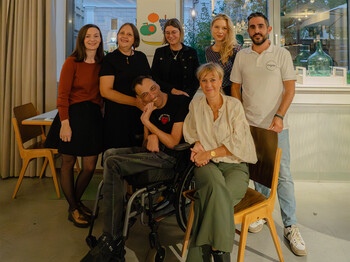 Künstler Günther Steiner in Begleitung bei der Vernissage, Galeristin Lena Freimüller (re), den Gastgeber*innen Lisa-Maria Tolazzi von der Caritas (1. von li. hinten) und magdas Geschäftsführer Salvatore Balsamo sowie Besucherinnen der Ausstellung.