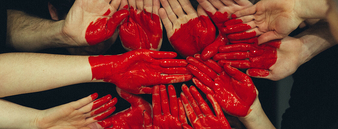 Viele Hände formen ein Herz auf das auch noch ein Herz in rot gemalt ist.