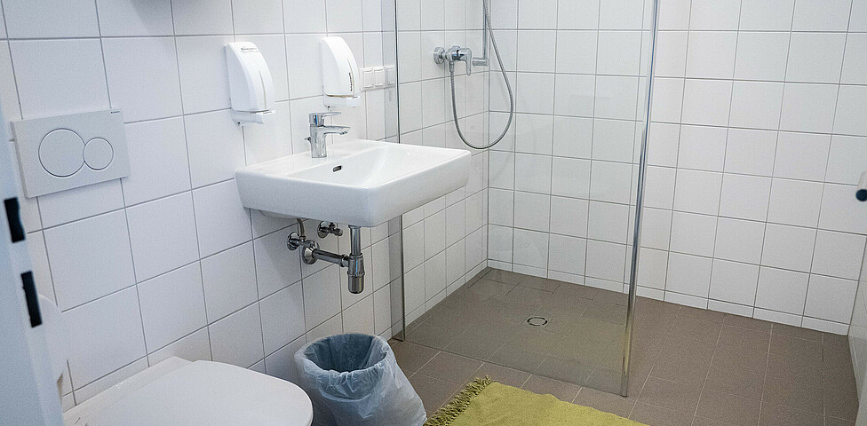 Die Sanitäranlagen der Notschlafstelle mit WC, Waschbecken und Spiegel sowie Dusche.