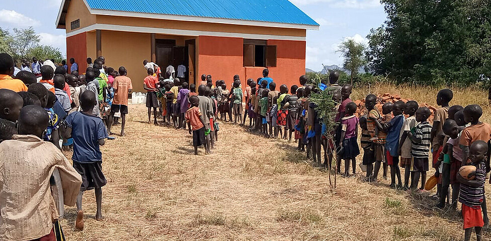 Die Schüler*innen der Schule in Locherep stehen vor der neu errichteten Küche in einer Reihe um sich das Mittagessen abzuholen. Die Schlange reicht bis an den Bildrand
