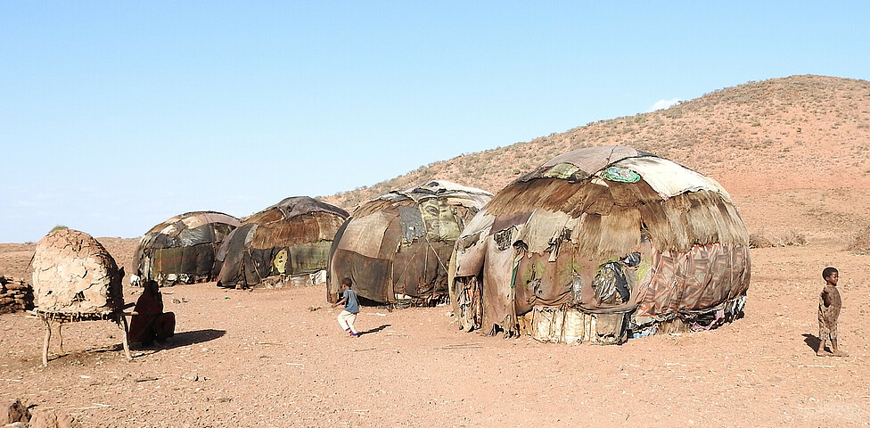Hütten der Nomaden in einer kahlen Landschaft ein Kind steht vor diesen Behausungen.