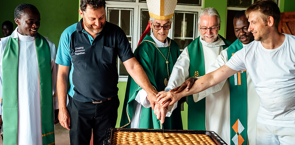 Der jetzige Bischof von Kärnten Josef Marketz und ein Bischof aus Uganda schneiden mit Projektförder*innen den ersten Kuchen der Bäckerei an.