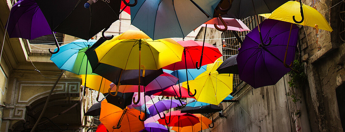 Viele bunte Regenschirme hängen an Leinen über einer Gasse.