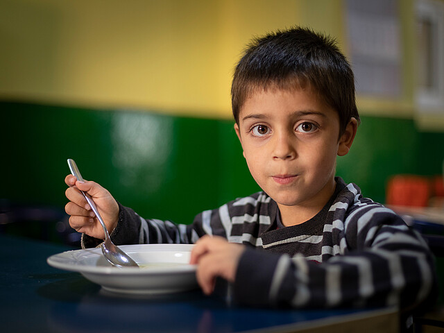 Ein Junge sitzt am Tisch und isst eine warme Suppe.