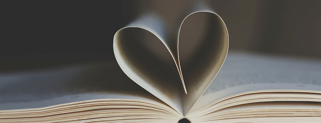 Ein geöffnetes Buch formt mit einigen Blättern ein Herz.