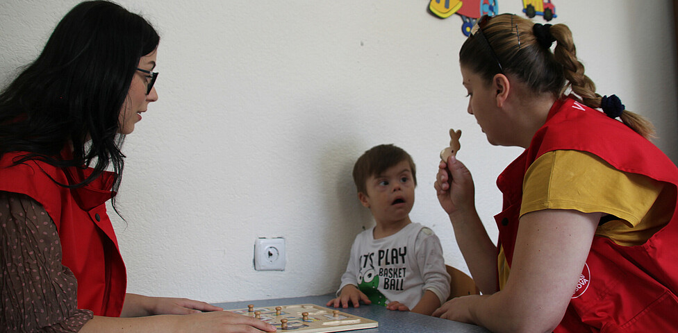Zwei Betreuerinnen lernen mit einem Kind die Namen der Tiere mit einem Holzspielzeug.