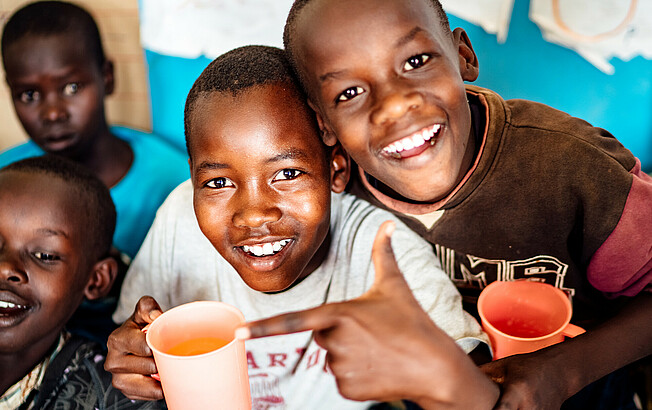 Eine Gruppe an Kindern in Afrika mit bunten Trinkbechern in der Hand lächeln.