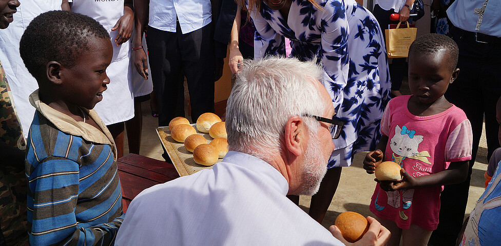 Der Kärntner Bischof Josef Marketz verteilt frisches Brot an die wartenden Kinder.