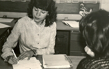 Ein schwarz-weiß Foto von einer Dame die eine Frau in der Sozialberatung berät.