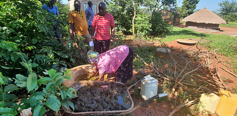 Eine Frau mischt in einer Schubkarre Kuhdung vor einem Gemüsefeld zusammen für die Biogasanlagen.