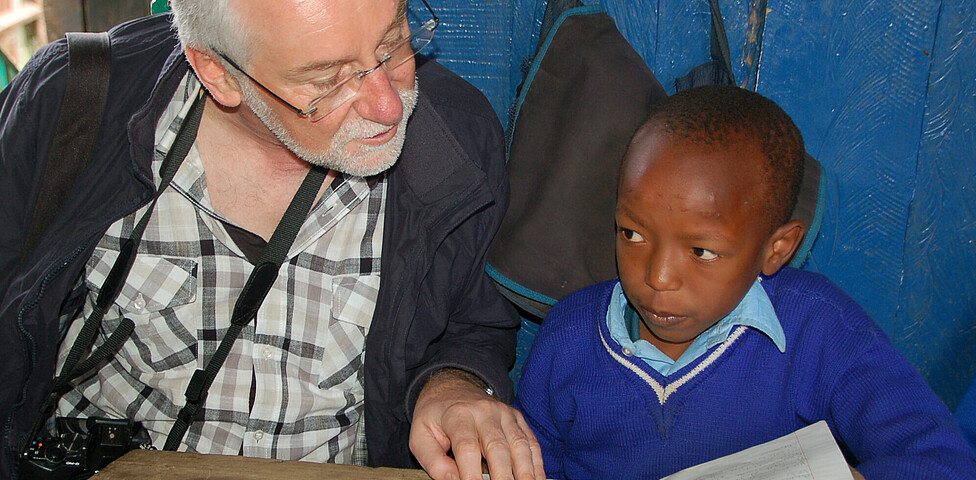 Caritasdirektor Marketz sitz neben einem Jungen und sie sehen sich gemeinsam ein Schulbuch an.