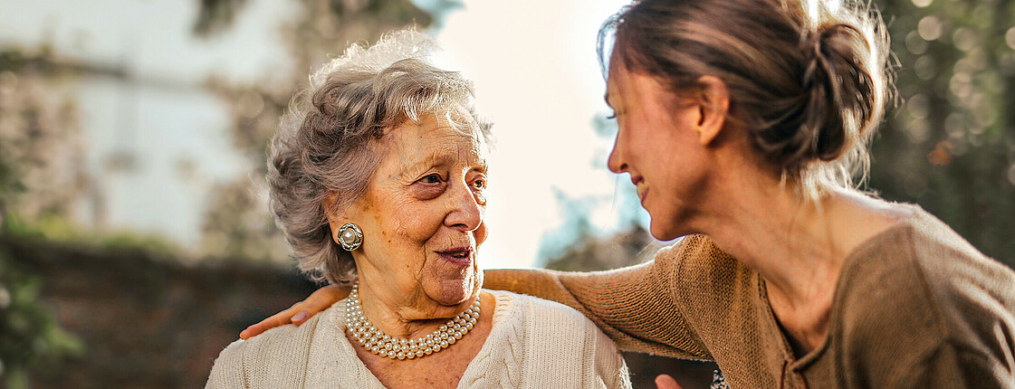 Eine junge Frau hält einer älteren Dame die Hand und hört ihr zu.