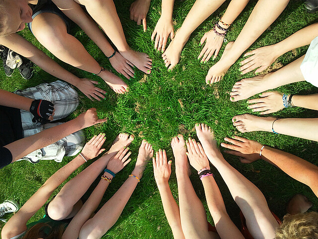 Viele Menschen stehen im Kreis und halten ihre Hände in die Mitte um einen Kreis zu formen.