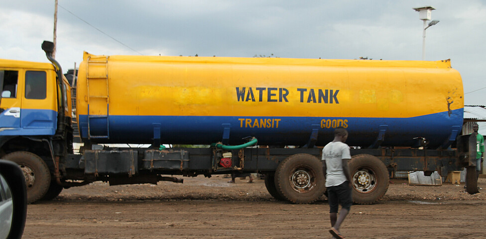 Ein großer Wassertank fährt über eine unbefestigte Straße.