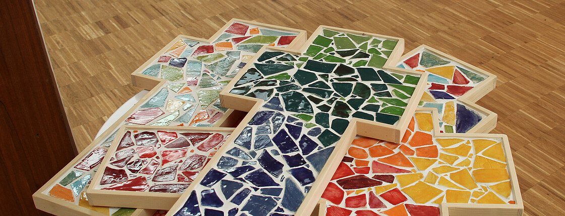 Holzkreuze mit bunten Mosaiksteinen befüllt liegen gestapelt aufeinander.der.