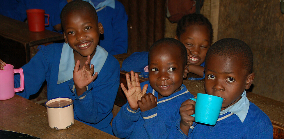Kindern lächeln mit der oft einizigen warmen Mahlzeit am Tag in die Kamera.