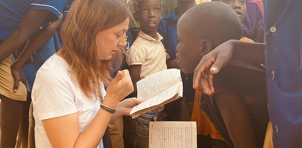 Die Bereichsleiterin Alexandra Blattnig-Rull der Auslandshilfe der Caritas Kärnten sitzt bei einem Projektbesuch umringt von Kindern der Schule und fragt diese wie es ihnen geht.