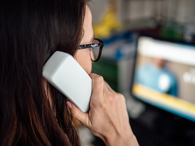 Eine Braunhaarige mit Brille hält einen Telefonhörer in der Hand und sieht dabei auf den Bildschirm, auf dem man die Website der Telefonseelsorge Österreich leicht verschwommen sieht.