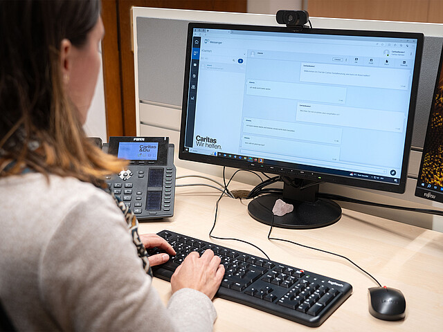Eine Beraterin sitzt an ihrem Schreibtisch und verwendet ihren Computer um mit einer Klientin zu chatten.