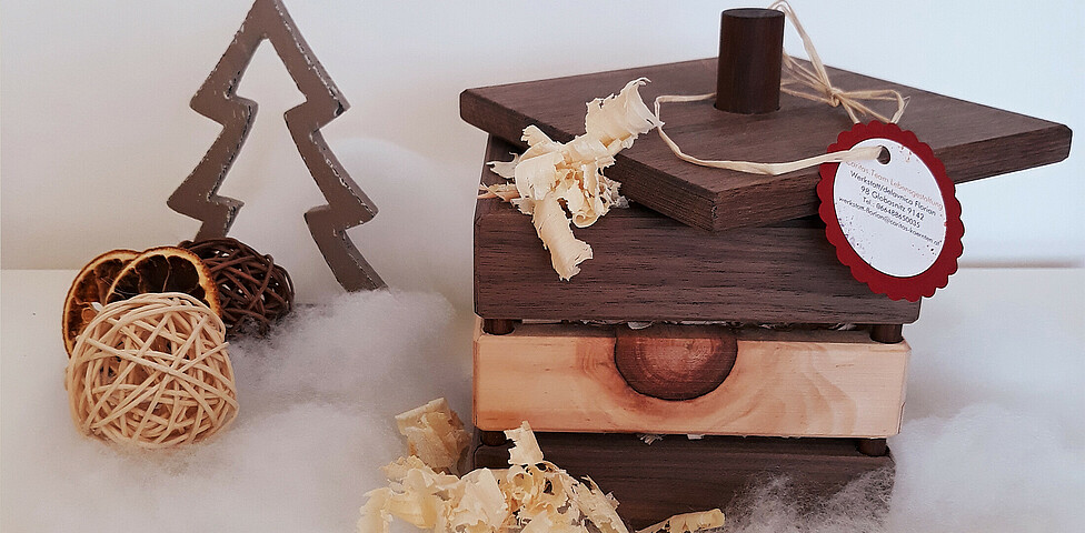 Eine braune Holzbox mit Zirbenspännen gefüllt auf Watte und vor einem weißen Hintergrund drapiert.