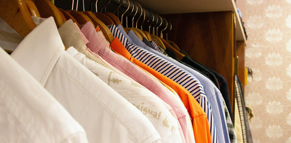 Mehrere Oberteile, vor allem Blusen und Hemden an einer Kleiderstange.