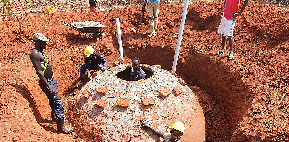 Arbeiter ziegeln die letzten Reihen der runden Biogasanlage, bei der ein Loch als Öffnung oben offen bleibt.