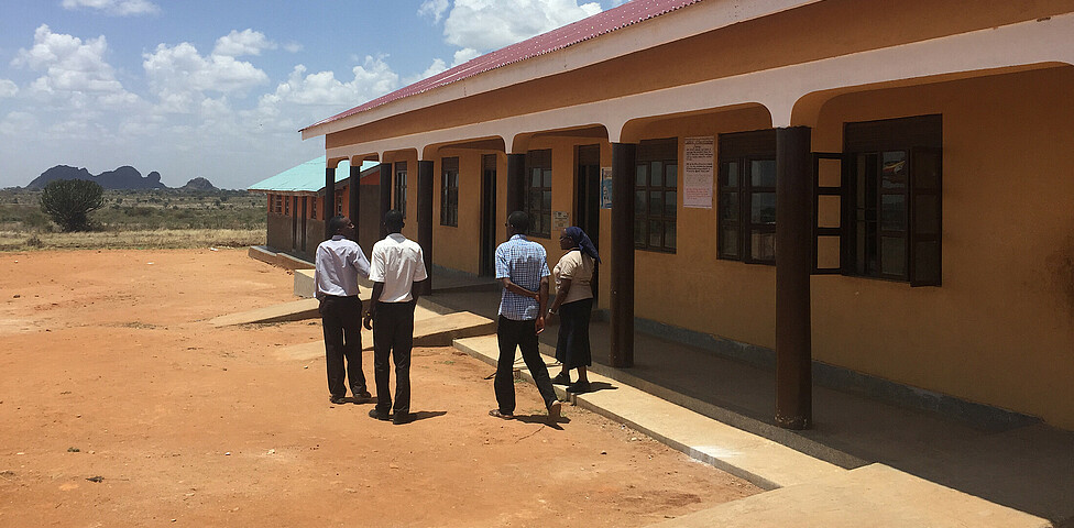 Die neuen Schulgebäude werden von vier jungen Männern besichtet.
