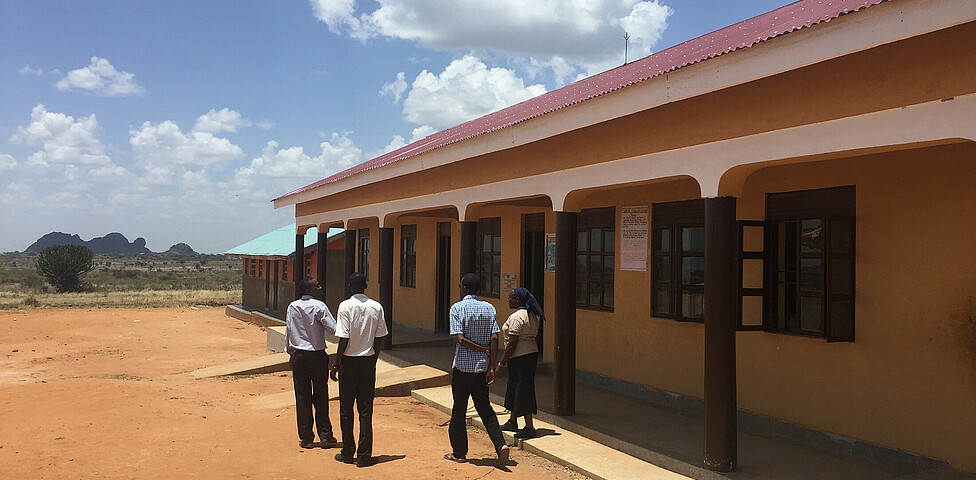 Die neuen Schulgebäude werden von vier jungen Männern besichtet.
