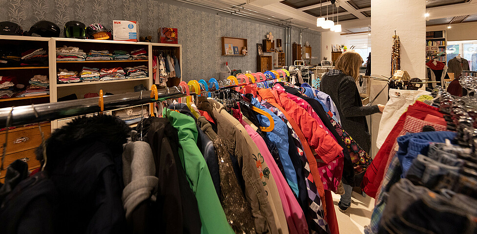 Winterkleidung vor allem dicke Winterjacken hängen an den Kleiderstangen im Geschäft. Eine Kundin sieht sich gerade ein Kleidungsstück an.
