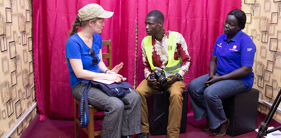 Projektreferentin Theresa Sacher sitzt mit einem Teilnehmer der Fotografie-Ausbildung von Kitgum in einem Fotosetting.