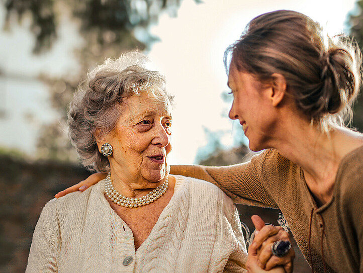Eine junge Frau hält einer älteren Dame die Hand und hört ihr zu.