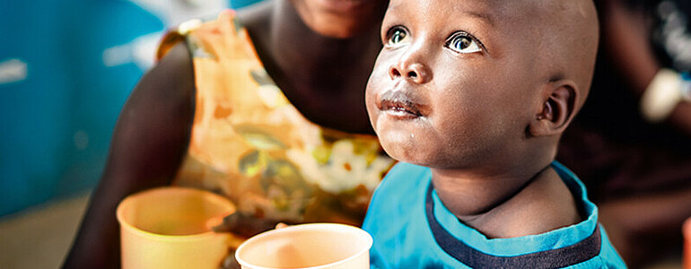 Zwei Kinder in Uganda haben einen Trinkbecher mit nahrhaften Brei in der Hand.