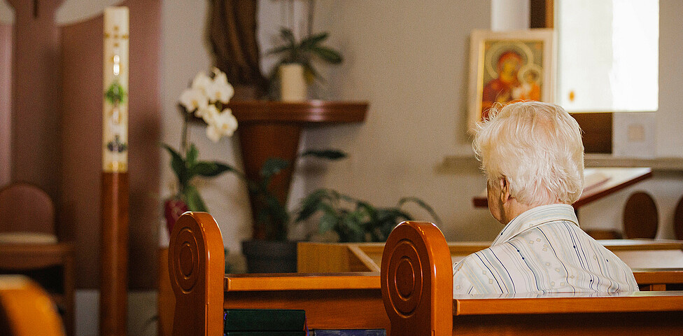 Eine Dame sitzt auf einer Kirchenbank mit dem Rücken zugekehrt und betet in der hauseigenen Kapelle.