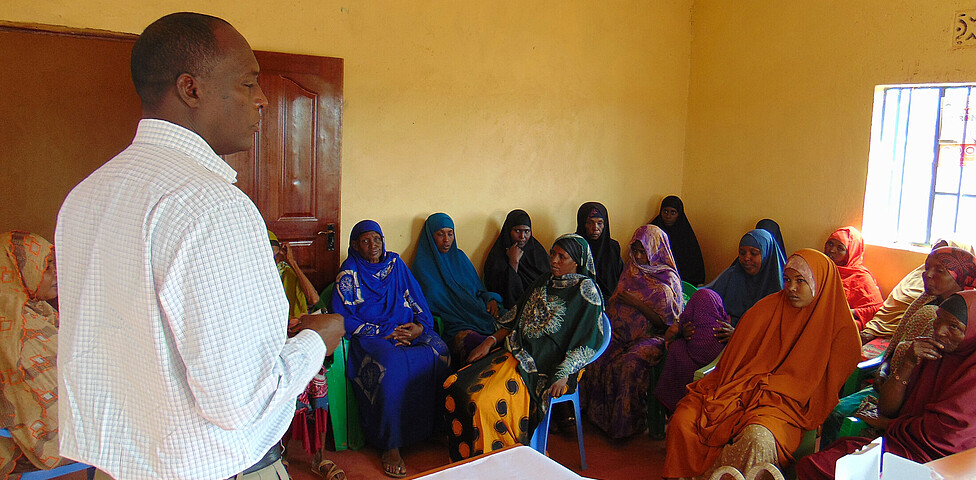 Frauen des Ortes Kinisa in Kenia sitzen in einem Gemeindegebäude und hören dem Projektleiter bei der Schulung zu.