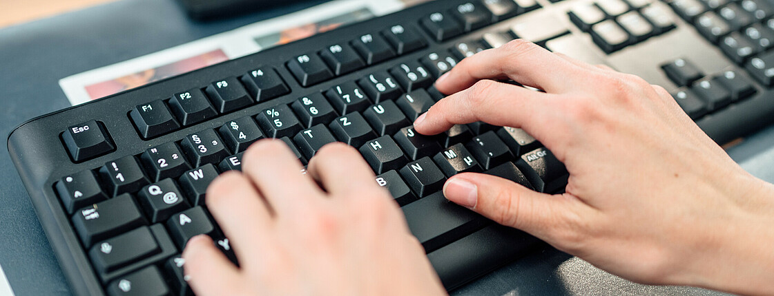 Frauenhände tippen etwas auf einer Computer-Tastatur ein.