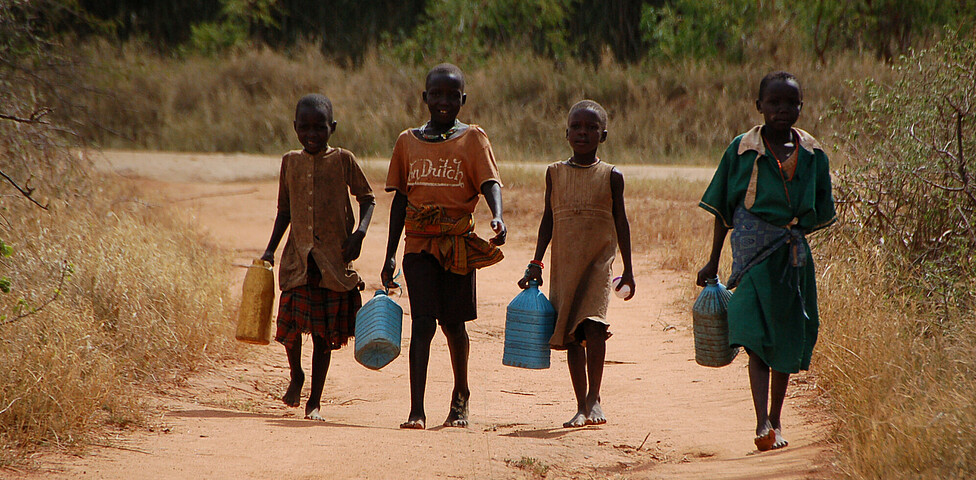 Vier Kinder mit vollen Wasserkanistern kommen den Weg entlang zurück.